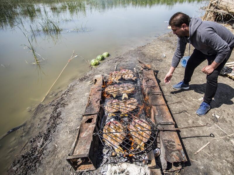 An Iraqi tourist grills fish by the marshes of the southern district of Chibayish in Dhi Qar province, about 120 kilometres northwest of the southern city of Basra, on March 29, 2019. Hussein FALEH / AFP