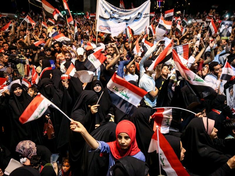 Iraqi followers of Shiite Muslim cleric Moqtada al-Sadr wave national flags and raise protest signs as they demonstrate in the capital Baghdad's central Tahrir Square late on May 24, 2019, against involvement in any conflict between Iran and the United States.  AHMAD AL-RUBAYE / AFP