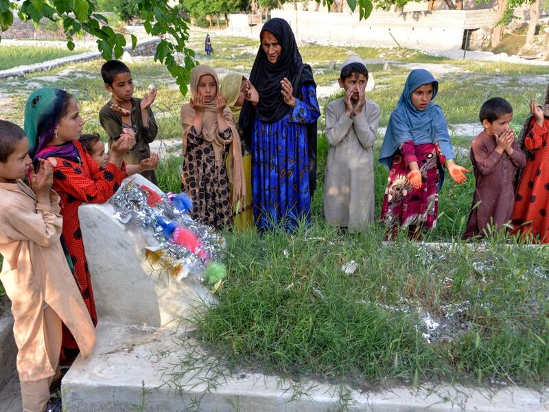 In this photograph taken on April 22, 2019, Afghan woman Niaz Bibi (C in blue), 70, and her orphaned grandchildren pray on the tombs of her sons and grandsons killed by ISIS militants in the Kot district of the Nangarhar province. NOORULLAH SHIRZADA / AFP