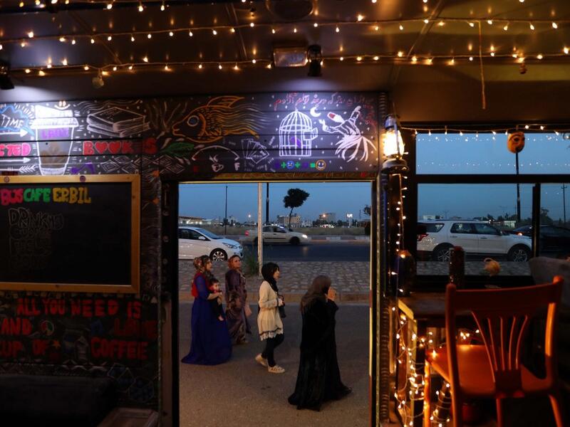 Muslim women walk past "The Bus Cafe Erbil" in Arbil, the capital of Iraq's Kurdish autonomous region late on June 7, 2019, on the long weekend of the Eid al-Fitr holiday which marks the end of the holy fasting month of Ramadan.  SAFIN HAMED / AFP