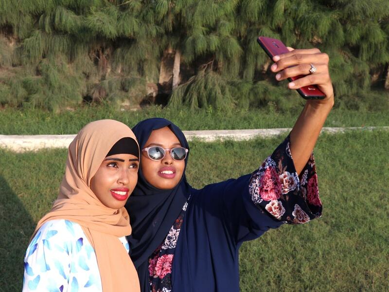 Rahma Abdullahi Mohamud (R) and Hani Hussein take selfies pictures with a mobile phone, after buying clothes designed by fashiondesigner Muna Mohamed Abdullahi, at Peace Garden in Mogadishu, Somalia. ABDI HAJJI HUSSEIN / AFP