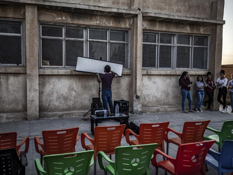 A member of Syrian-Kurdish filmmaker Shero Hinde's mobile cinema "Komina Film" initiative prepares a projector screen for a film screening for children at a school yard in the village of Shaghir Bazar, 55 kilometres southest of Qamishli in the Kurdish-populated areas of northeastern Syria's Hasakeh province, on July 28, 2019.  DELIL SOULEIMAN / AFP