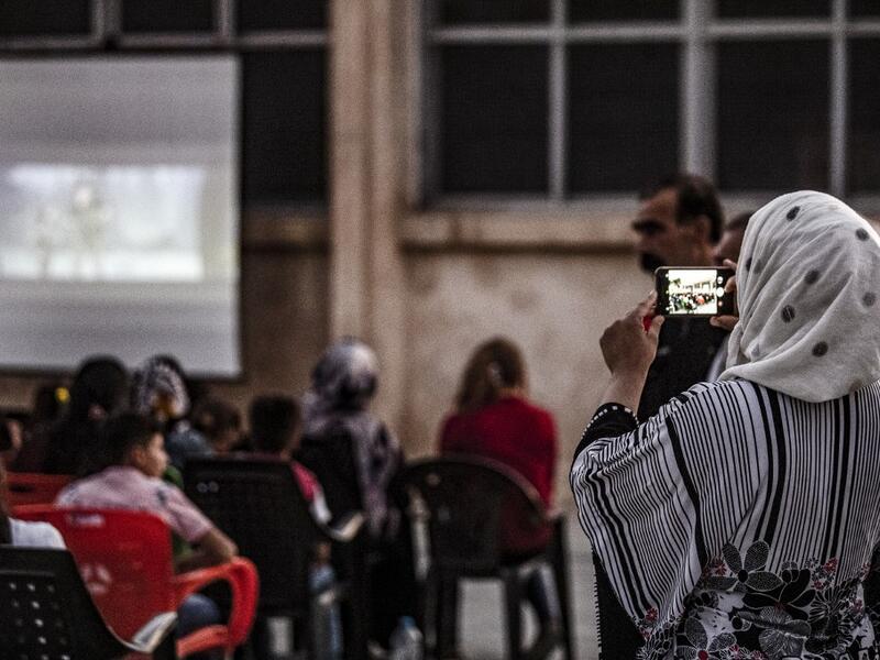 A woman uses a cell phone to shoot a video of children attending a film screening as part of the mobile cinema "Komina Film" initiative organised by Syrian-Kurdish filmmaker Shero Hinde, at a school yard in the village of Shaghir Bazar, 55 kilometres southest of Qamishli in the Kurdish-populated areas of northeastern Syria's Hasakeh province, on July 28, 2019. DELIL SOULEIMAN / AFP