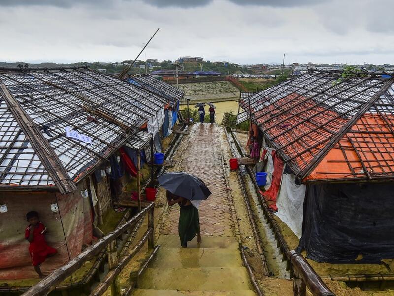A Rohingya refugee girl shelters from the rain under an umbrella as she makes her way back home after collecting relief aid at the Kutupalong Rohingya refugee camp in Bangladesh's Ukhia district on August 24, 2019.  MUNIR UZ ZAMAN / AFP