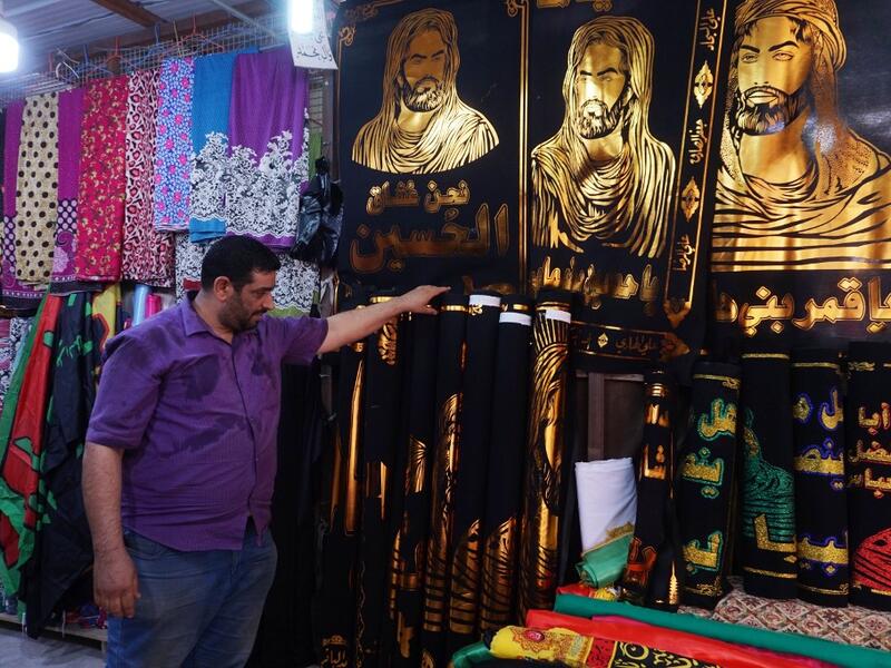 A man stands next to cloth banners depicting Shiite Muslim Imams Hussein ibn Ali (L and C) and his brother Abbas ibn Ali (R), grandsons of the prophet Mohammed, to be sold amidst preparations ahead of the Shiite Muslim religious mourning period of Ashura, in the central Iraqi holy shrine city of Najaf on August 31, 2019.  Haidar HAMDANI / AFP