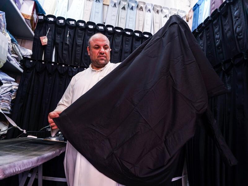 A man showcases a black garb in a shop lined-up with black and other coloured shirts, to be sold to Shiite Muslim pilgrims amidst preparations ahead of the Shiite religious mourning period of Ashura in the central Iraqi holy shrine city of Najaf on August 31, 2019.  Haidar HAMDANI / AFP