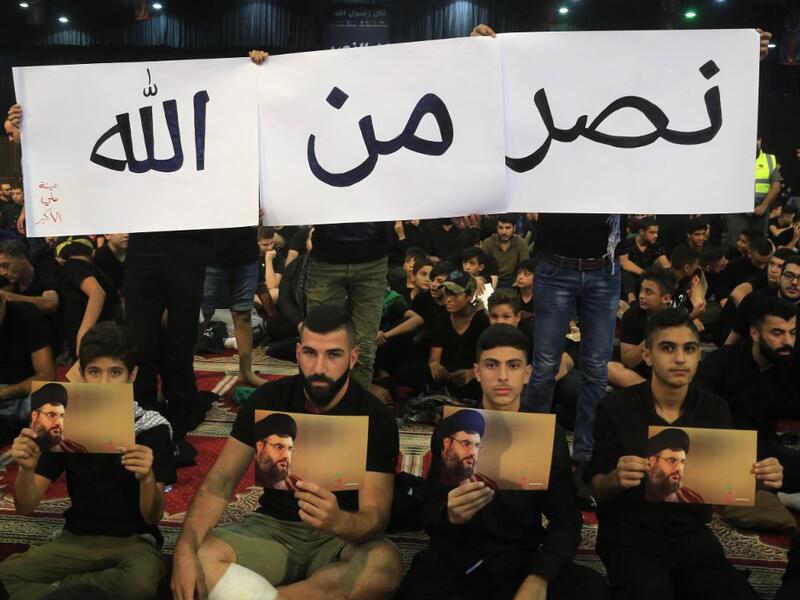Supporters of the Lebanese Shiite Hezbollah movement hold pictures of the leader Hasan Nasrallah as they watch his speech, transmitted on a large screen in the Lebanese capital Beirut's southern suburbs, on September 2, 2019. (AFP/ File Photo)