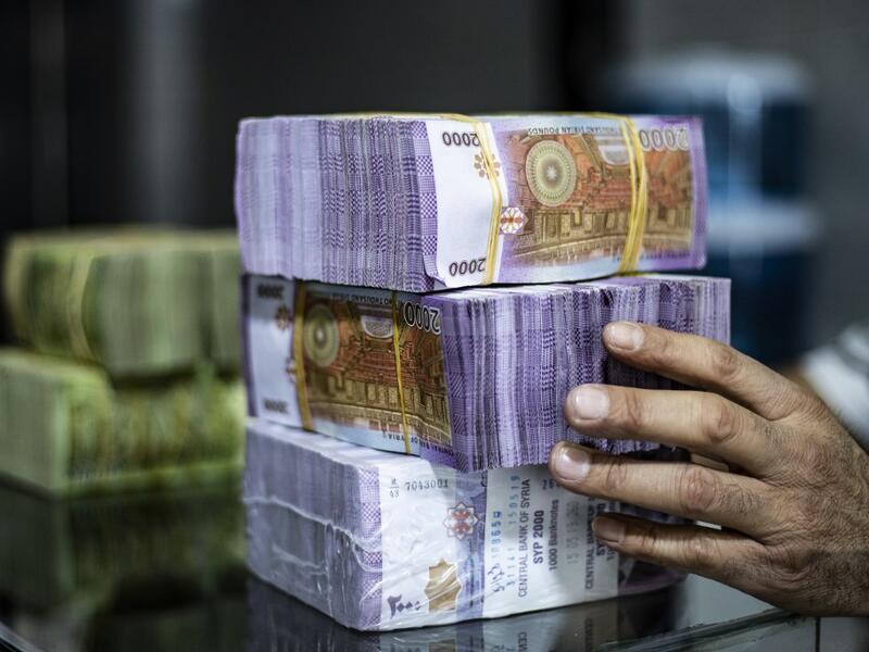 A merchant arranges stacks of Syrian pounds at a market in the Kurdish-majority city of Qamishli in northeast Syria on September 10, 2019. The declining value of the pound is a sure sign of Syria's ailing economy. The civil war has battered the country's finances and depleted its foreign reserves. A flurry of international sanctions on President Bashar al-Assad's regime and associated businessmen since the start of the war in 2011 has compounded the situation.  Delil SOULEIMAN / AFP
