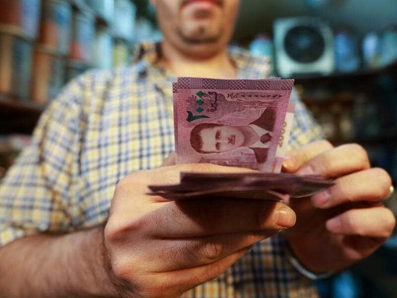 A merchant counts Syrian pound notes, bearing a portrait of the Syrian President Bashar al-Assad, at the Bzourieh market in the centre of the Syrian capital Damascus.  LOUAI BESHARA / AFP
