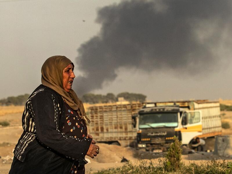 A woman walks as smoke billows following Turkish bombardment in Syria's northeastern town of Ras al-Ain in the Hasakeh province along the Turkish border on October 9, 2019. Turkey launched an assault on Kurdish forces in northern Syria with air strikes and explosions reported along the border. President Recep Tayyip Erdogan announced the start of the attack on Twitter, labelling it "Operation Peace Spring".  Delil SOULEIMAN / AFP
