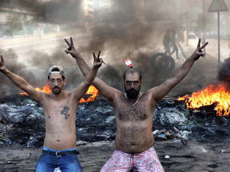 Lebanese demonstrators gesture as tires burn during a protest against dire economic conditions in the industrial zone of Dora on the northern outskirts of Beirut (AFP)