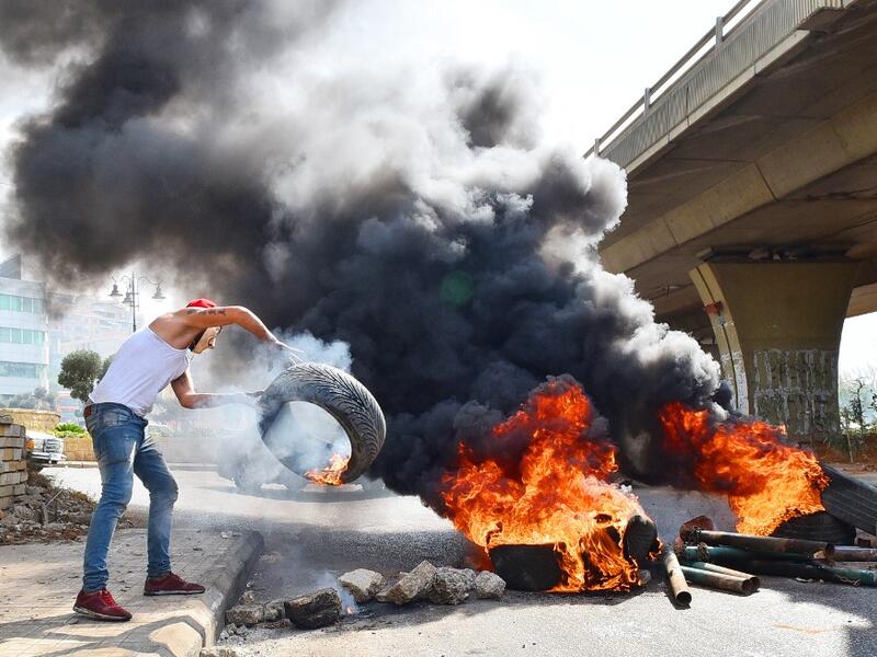 A Lebanese protester throws a tire into a fire blocking a road near Beirut-Rafic Hariri International Airport, amidst ongoing protests against dire economic conditions, on October 18, 2019. Public anger has simmered since parliament passed an austerity budget in July to help trim a ballooning deficit and flared on October 17 over new plans to tax calls on messaging applications such as WhatsApp, forcing the government to axe the unpopular proposal. AFP
