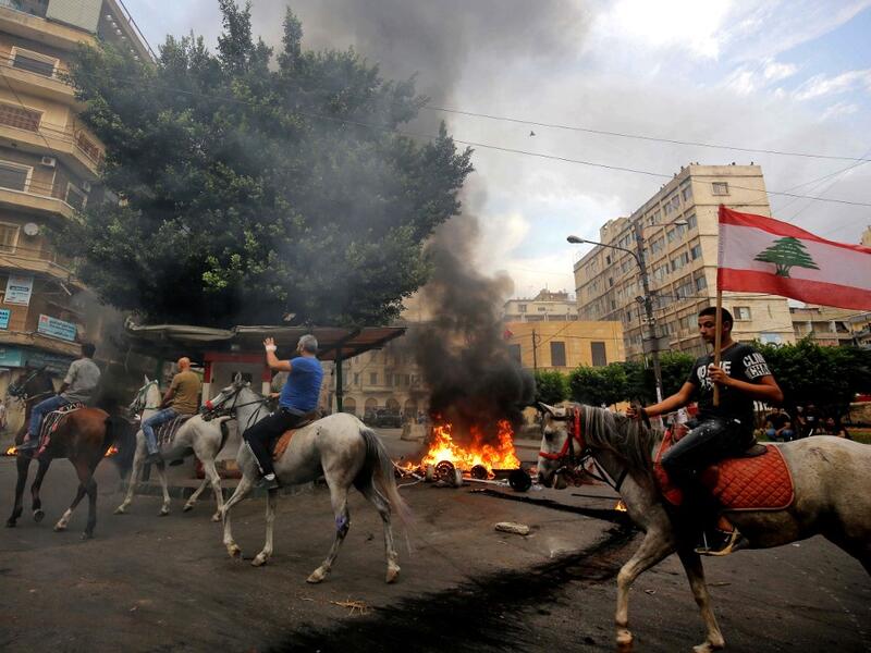 Lebanese protesters ride horses past burning tires in front of the house of former sports minister Faisal Karami, during a protest against dire economic conditions in the coastal city of Tripoli to the north of Beirut, Lebanon on October 18, 2019 Ibrahim CHALHOUB / AFP