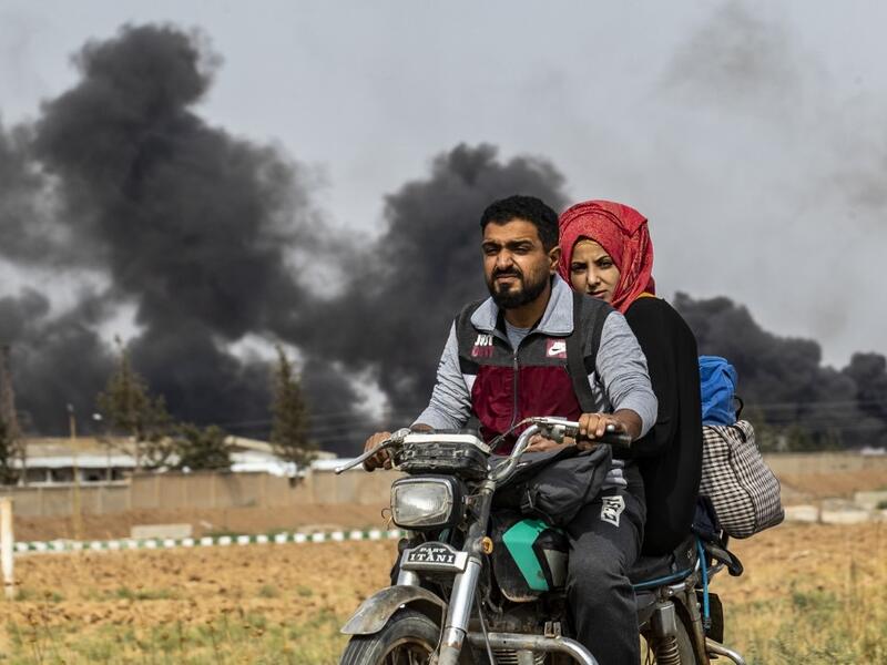 A Syrian couple use a motorcycle to flee the countryside of the northeastern Syrian town of Ras al-Ain on the Turkish border, toward the west to the town of Tal Tamr on October 19, 2019. The smoke behind them is from burning tyres used to impede visibility from warplanes. Delil SOULEIMAN / AFP