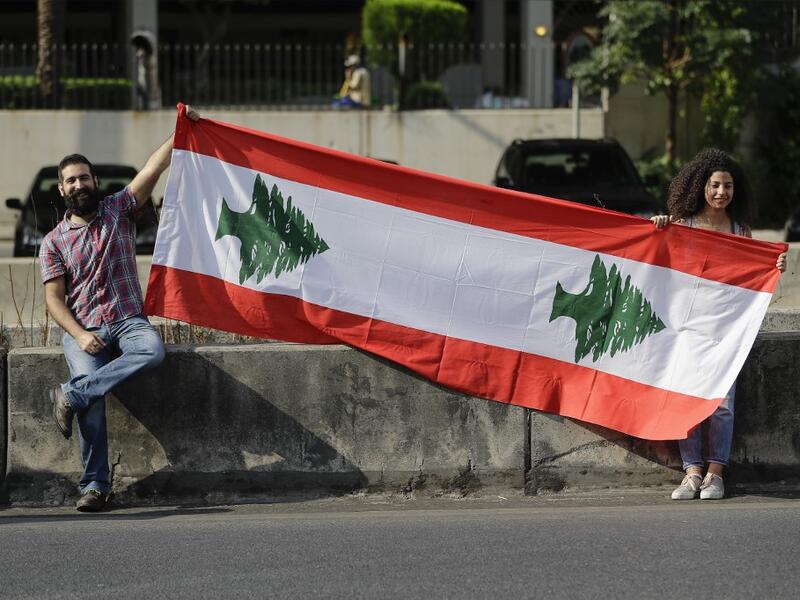 Lebanese protesters hold a national flag as they participate in forming a human chain along the coast from north to south as a symbol of unity, during ongoing anti-government demonstrations in Nahr al-Kalb north of Lebanon's capital Beirut on October 27, 2019. JOSEPH EID / AFP