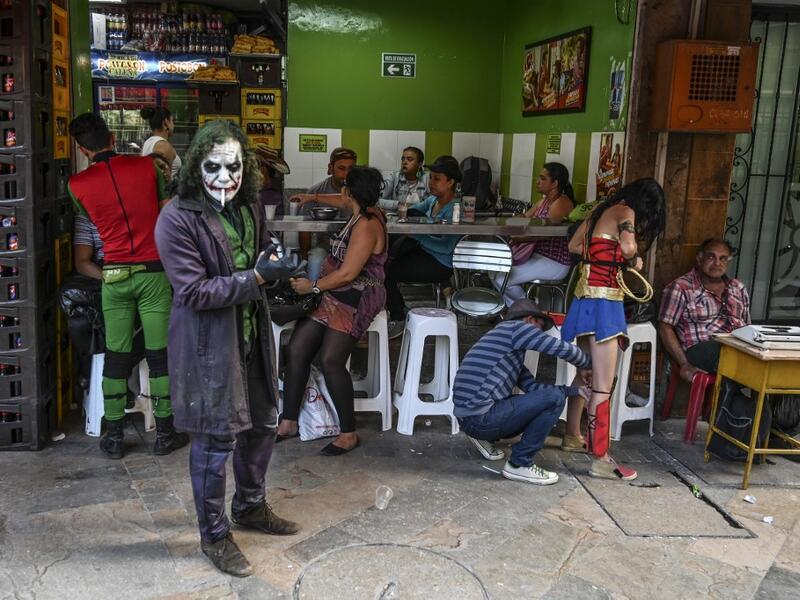 Venezuelan migrant Johnny Tales (L), who makes a living imitating the comicbook and film character "The Joker", smokes a cigarette as fellow compatriots also fancy dressed as comic and film industry characters prepare to perform in Medellin, on October 29, 2019. JOAQUIN SARMIENTO / AFP