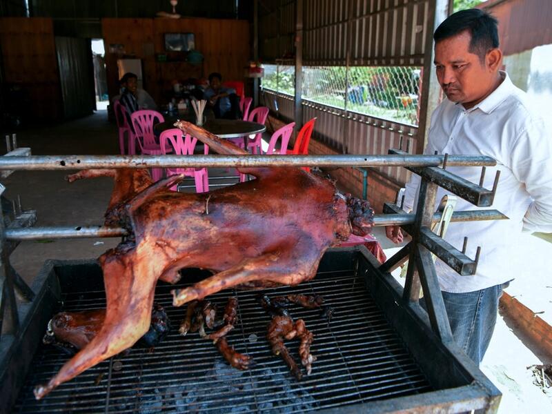 This photo taken on October 26, 2019 shows a man looking at a grilled dog at a restaurant in Kampong Cham province. Cambodian dog meat traders drown, strangle and stab thousands of canines a day in a shadowy but sprawling business that traumatises workers and exposes them to deadly health risks like rabies. TANG CHHIN Sothy / AFP