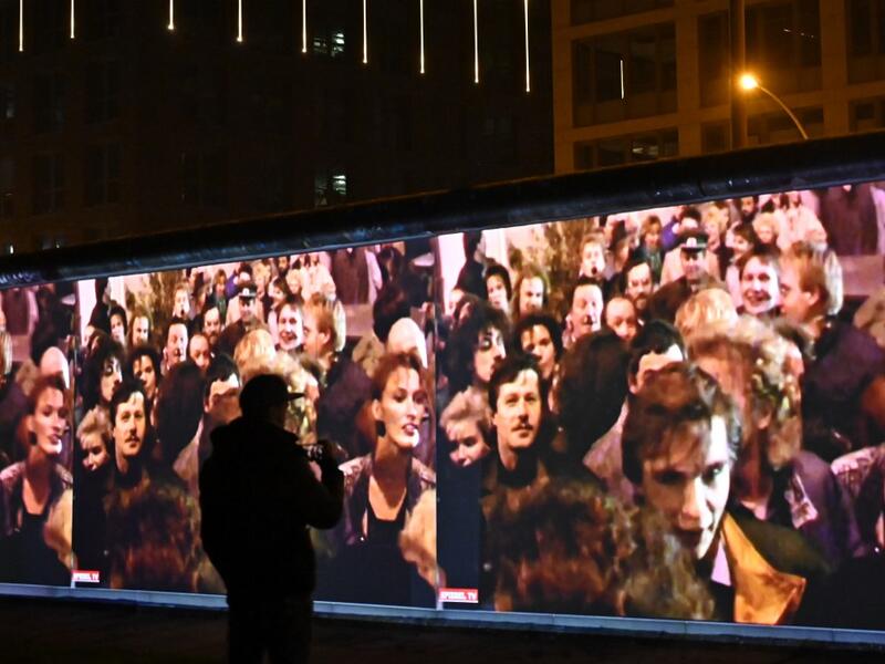 A spectators stands in front of a 3D video installation projected on the so-called East Side Gallery, a 1,3 km-long portion of the Berlin wall, during a rehearsal on November 3, 2019 in Berlin.  Tobias SCHWARZ / AFP