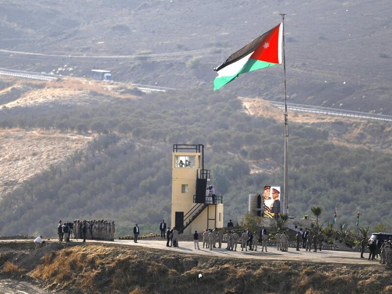 A picture taken from the Israeli side of the border shows King Abdullah II of Jordan (L) standing to attention with army troops under a Jordanian national flag during a ceremony at the Jordan Valley site of Naharayim, also known as Baqura, east of the Jordan River on November 11, 2019. (AFP/ File Photo)