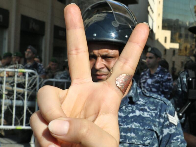 A Lebanese protester flashes the victory gesture while standing before a riot policeman at a security barrier across a road leading to the parliament headquarters during a demonstration in the capital Beirut's downtown district on November 19, 2019. An unprecedented protest movement against the ruling elite entered its second month with the country in the grip of political and economic turmoil. The leaderless pan-sectarian movement has swept the Mediterranean country since October 17, prompting the resignat