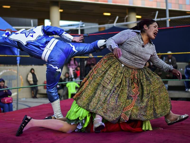 Bolivian wrestler Ana Luisa Yujra (R), aka "Jhenifer Two Faces", Lidia Flores (on the canvas), aka "Dina, The Queen of the Ring", both members of the Fighting Cholitas, and a wrestler fight at Sharks of the Ring wrestling club in El Alto, Bolivia, on November 24, 2019. After a fortnight hiatus due to anti-government protests and blockades, the Fighting Cholitas are back in the ring. The unrest was triggered by the disputed October 20 election, which Evo Morales claimed to have won and opposition groups said