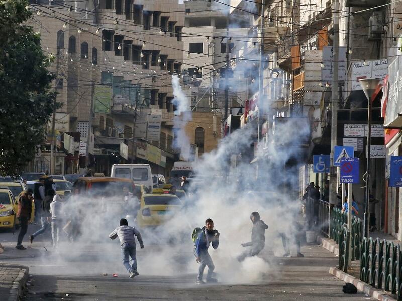 Palestinian youths run from tear gas smoke fired by Israeli security forces on November 26, 2019 during clashes in the West Bank city of Hebron during a Palestinian "day of rage" against a recent US decision to no longer consider settlements in the West Bank illegal. A Palestinian convicted over the killing of three Israelis died of cancer in custody today, officials said. The death, which sparked Palestinian accusations of neglect, comes amid heightened tension with protests already scheduled in multiple p