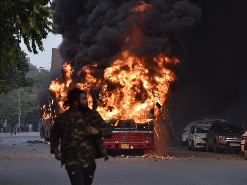 A man walks on a street as a bus is on fire following a demonstration against the Indian government's Citizenship Amendment Bill (CAB) in New Delhi on December 15, 2019. Angry protesters in northeast India vowed on December 15 to keep demonstrating against a contentious citizenship law as the death toll from bloody clashes opposing the bill rose to six. STR / AFP