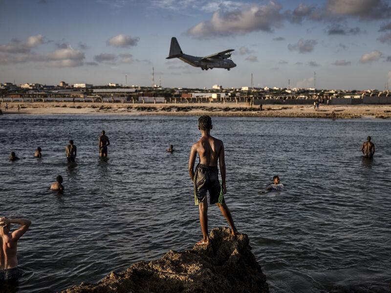Soldiers enjoying a day off and Somali people look from the beach at a military plane landing within Mogadishu’s airport base in Mogadishu, Somalia, on December 13, 2019. LUIS TATO / AFP