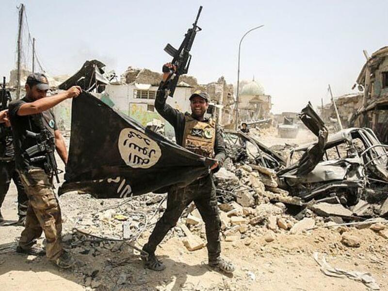 Members of the Iraqi Counter-Terrorism Service cheer in Mosul as they carry upside-down Islamic State flag, with the destroyed Al-Nuri mosque seen in the background on July 2, 2017 (AFP)