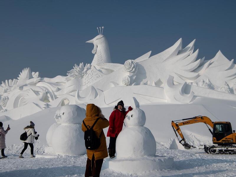 Tourist pose in front of an ice sculpture ahead of the opening of the Harbin International Ice and Snow Festival in Harbin, in China's northeast Heilongjiang province on January 4, 2020. NOEL CELIS / AFP