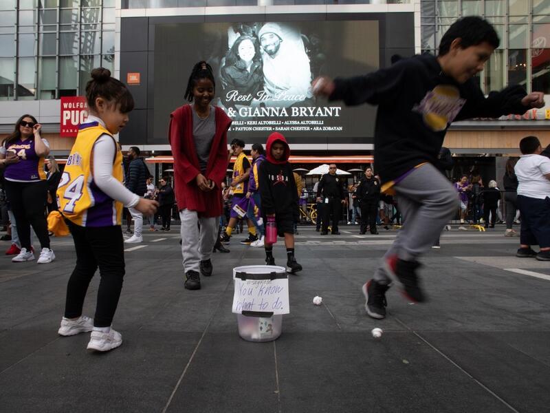 Children plays basket with paper balls in a trash can in front of a makeshift memorial for former NBA and Los Angeles Lakers player Kobe Bryant and his daughter Gianna Bryant, who were killed with seven others in a helicopter crash on January 26, at LA Live plaza in front of Staples Center in Los Angeles on January 27, 2020. Federal investigators sifted through the wreckage of the helicopter crash that killed basketball legend Kobe Bryant and eight other people, hoping to find clues to what caused the accid