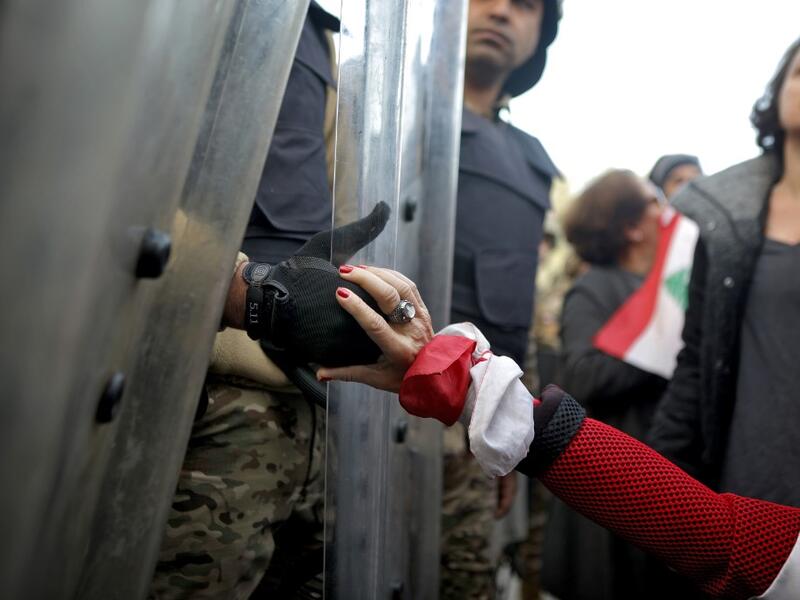 A Lebanese anti-government protester holds the hand of a Lebanese army soldier as she blocks a road leading to the parliament in the capital Beirut's downtown district on January 27, 2020 PATRICK BAZ / AFP