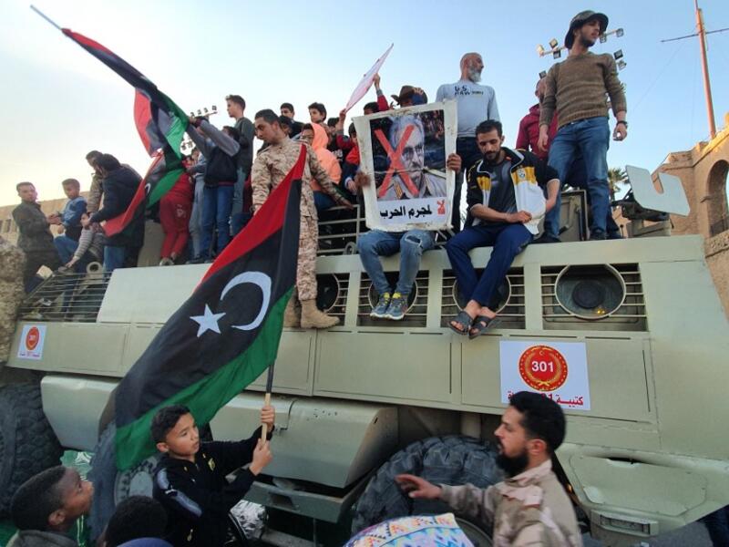 A man holds up a sign showing the face of Libyan strongman Khalifa Haftar with a red "X" above him and a caption in Arabic reading "no to the war criminal". AFP
