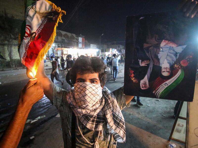 In this file photo taken on September 07, 2018, an Iraqi protester holds up an Iranian flag as another sets it on fire for him, next to a portrait depicting Iran's former and current Supreme Leaders Ayatollah Khomeini and Khamenei, during demonstrations against the government and the lack of basic services in Basra. Mocking clerics, falling in love at rallies and mending a broken society: even if Iraq's young protesters have failed to overthrow entrenched politicians, they have scored by shattering decades-