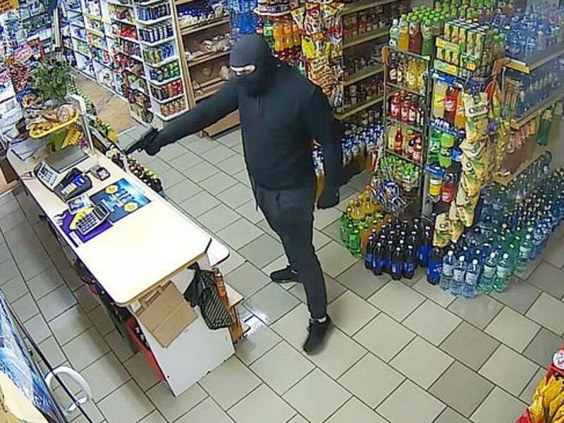 The man, who was seen wearing a balaclava, entered the shop before pulling out a gun and approaching the woman as she mopped the floors. (Video Screenshot)