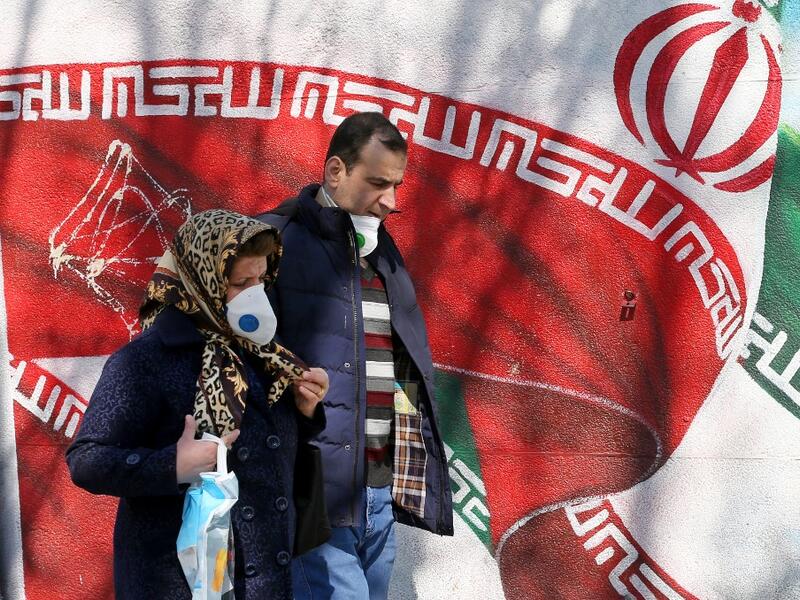Iranians wearing masks walk past a mural displaying their national flag in Tehran on March 4, 2020. Iran has scrambled to halt the rapid spread of the COVID-19 virus, shutting schools and universities, suspending major cultural and sporting events, and cutting back on work hours.  ATTA KENARE / AFP