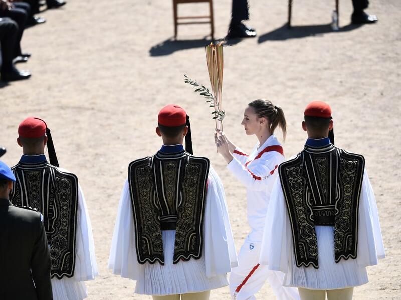 Torchbearer Greece's Anna Korakaki, Rio 2016 gold medallist in the 25m pistol shooting, walks past Greek Evzones Guard as she holds the Olympic flame and an olive branch during the flame lighting ceremony on March 12, 2020 in ancient Olympia, ahead of the Tokyo 2020 Olympic Games. ARIS MESSINIS / AFP