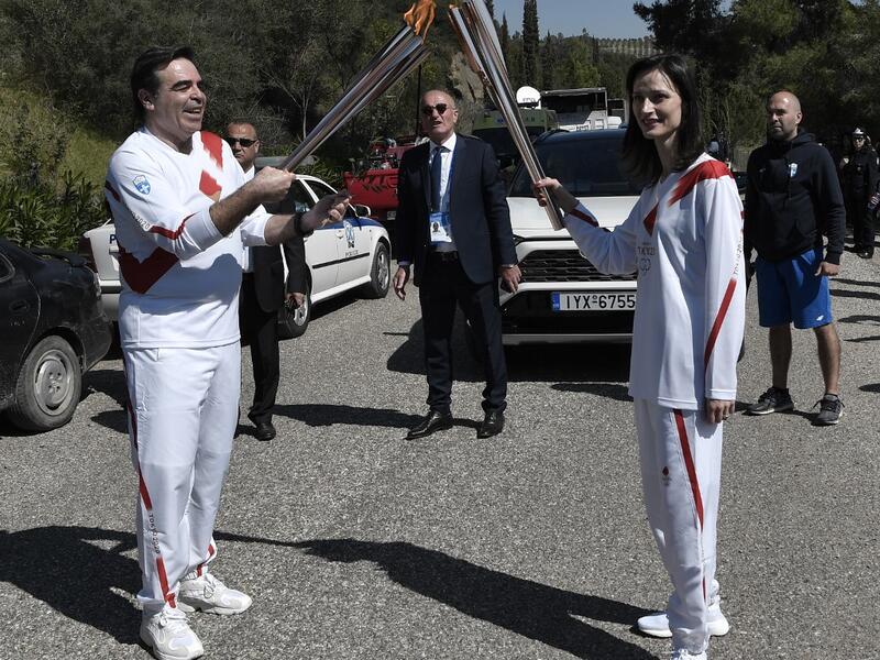 European Commission vice-president in charge for promoting our European way of life Margaritis Schinas (L) holds the Olympic flame during the flame lighting ceremony on March 12, 2020 in ancient Olympia, ahead of the Tokyo 2020 Olympic Games. LOUISA GOULIAMAKI / AFP