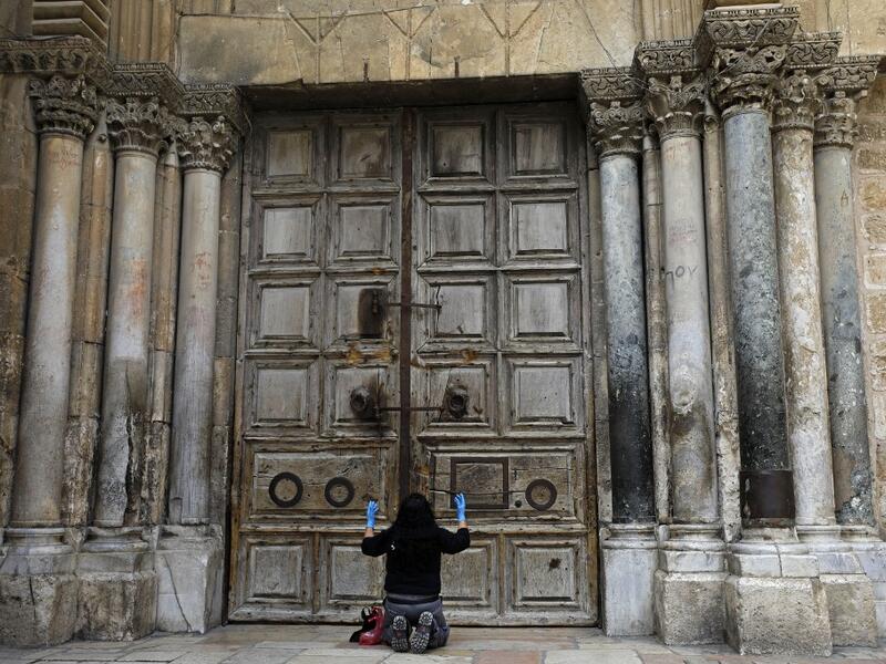 A woman prays in front of the Church of the Holy Sepulchre in the Old City of Jerusalem following the closure of the city for non-residents as a measure to contain the spread of the novel coronavirus, on March 30, 2020. MENAHEM KAHANA / AFP
