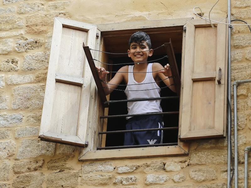 A Lebanese boy smiles as he looks out of a window during confinement at home due to the COVID-19 pandemic, in the historic part of the southern coastal city of Sidon (Saida), on April 6, 2020. Lebanon's President called on international donors to provide financial assistance to the crisis-hit country as it grapples with a severe economic downturn compounded by the novel coronavirus pandemic. JOSEPH EID / AFP