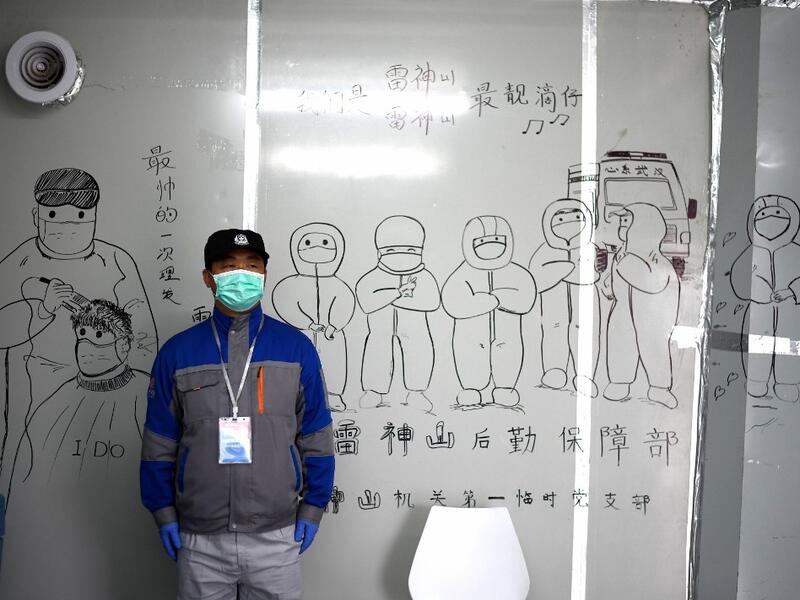 A security personnel stands in front of coronavirus themed drawings seen on a wall at the Leishenshan Hospital that had offered beds for coronavirus patients in Wuhan, in China’s central Hubei province on April 11, 2020. Noel Celis / AFP