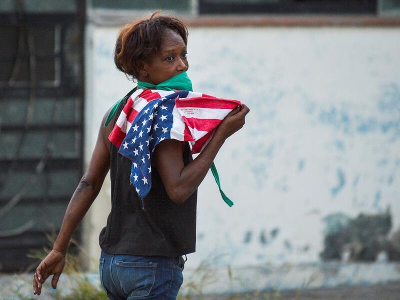 A woman wearing a face mask holds a US flag as she walks along a street in Havana, on April 13, 2020. While Cuba tries to stop the spread of the coronavirus on the island, with 726 cases, voices can be heard to demand the lifting of the US embargo to facilitate the arrival of medical products. YAMIL LAGE / AFP