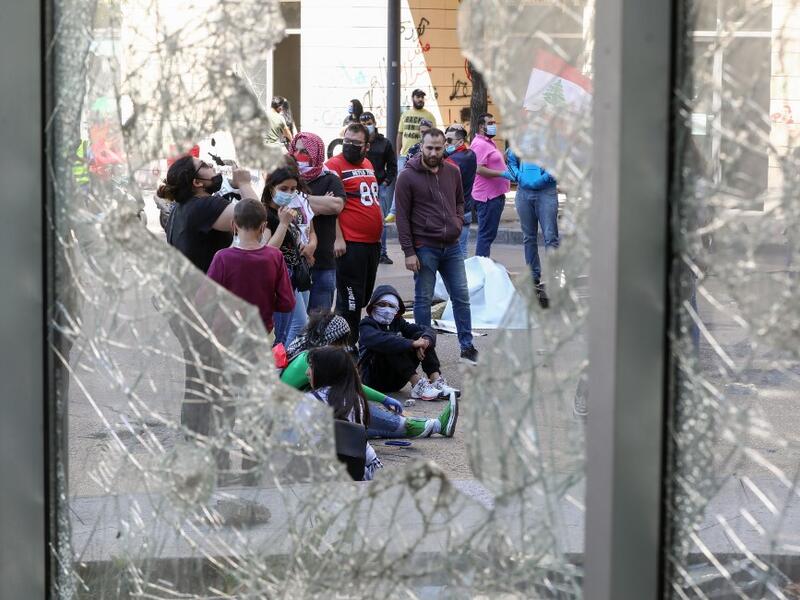 Lebanese anti-government protesters, some wearing protective masks amid the COVID-19 pandemic, are seen through a broken store window during a demonstration against the growing economic hardship in downtown Beirut on May 1, 2020, marking International Workers' Day (Labour Day). ANWAR AMRO / AFP