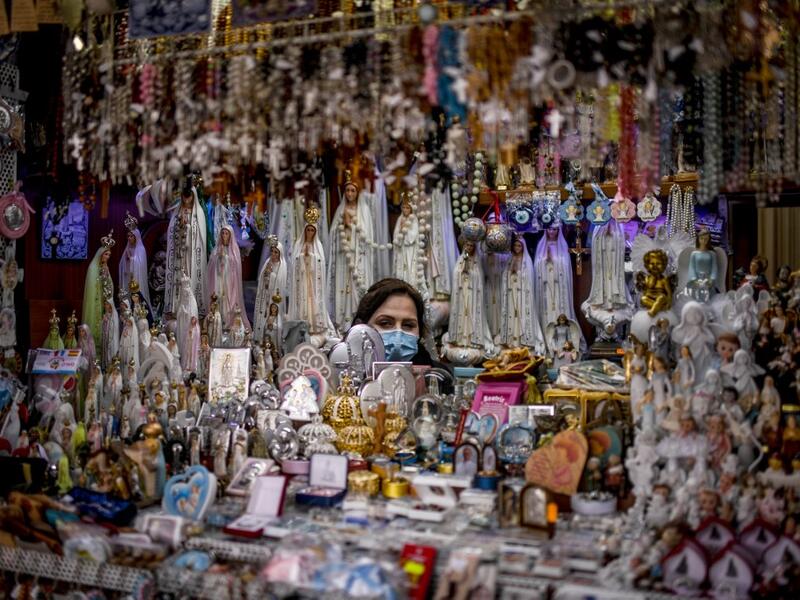 A seller of religious figurines poses at her stall wearing a face mask during the 103rd anniversary of the apparitions of Our Lady of Fatima at the Fatima shrine in central Portugal on May 13, 2020. Without the crowd of pilgrims it welcomes every year, the shrine of Fatima celebrated the anniversary during a religious ceremony reduced to the bare minimum. PATRICIA DE MELO MOREIRA / AFP