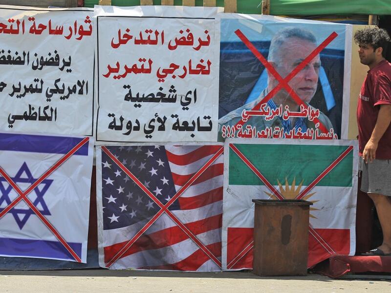 An Iraqi man stands next to the crossed flags of Israel (L), the US and Kurdistan (R) at a protest site along with slogans in Arabic denouncing foreign intervention in Iraq, at Al-Jumhuriyah bridge in the capital Baghdad on May 14, 2020. AHMAD AL-RUBAYE / AFP