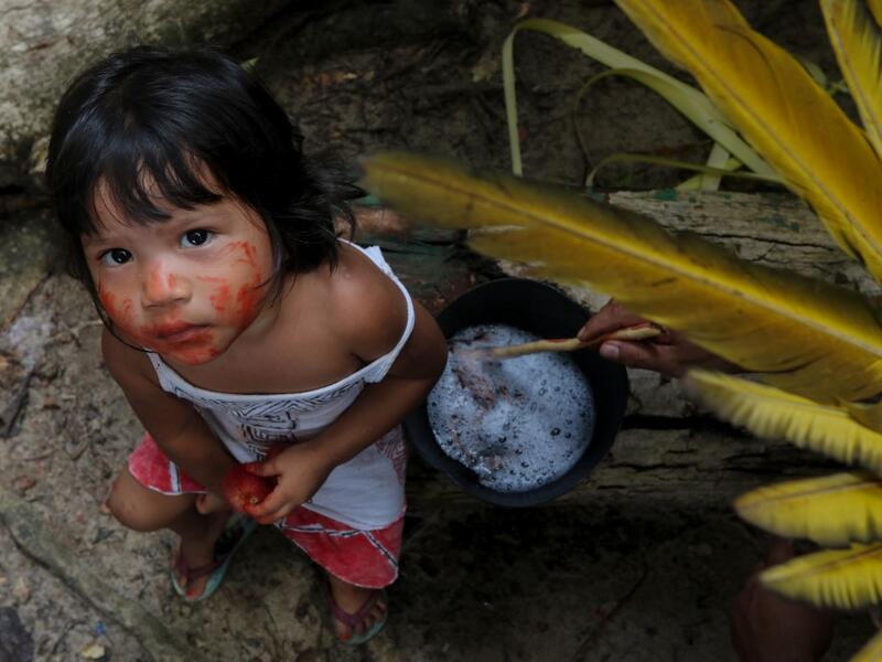 A Satere-Mawe indigenous child sits beside an man preparing medicinal herbs to treat people with symptoms of COVID-19 in the Wakiru community, in Taruma neighbourhood, a rural area west of Manaus, Amazonas State, Brazil, on May 17, 2020, during the novel coronavirus pandemic. Ricardo OLIVEIRA / AFP