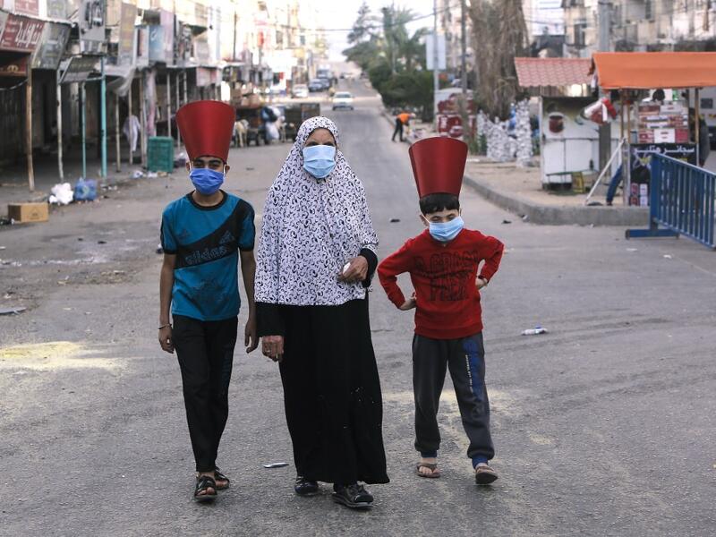 A Palestinian woman and paper-hat-clad children, wearing masks due to the COVID-19 coronavirus pandemic, walk along a street in Gaza City early on May 24, 2020, after performing prayers on the first day of Eid al-Fitr, the Muslim holiday which starts at the conclusion of the holy fasting month of Ramadan. Local authorities in the Hamas-run Palestinian enclave allowed mosques to reopen for Eid al-Fitr as social distancing procedures for the novel coronavirus are maintained while encouraging the elderly to pe