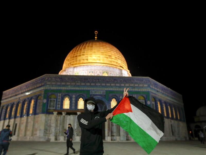 A Palestinian youth waves a national flag in front of the Dome of Rock at the Al-Aqsa Mosque compound, before the start of the dawn prayer (salat al-fajr) inside the compound in Jerusalem's Old City, on May 31, 2020, after a two-month closure due to the COVID-19 pandemic. AHMAD GHARABLI / AFP