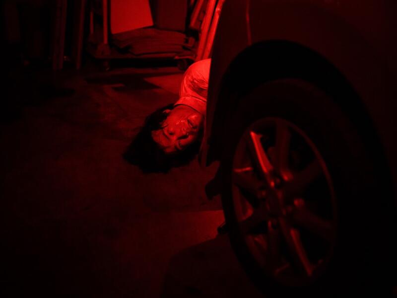 This picture taken on June 15, 2020 shows actor Kota Hanegawa, 28, acting as a victim during a demonstration of a haunted house at a garage in Tokyo. A car horn beeps and the horror begins: a bloody murder and rampaging zombies. But this drive-in haunted house in Japan protects against the most terrifying enemy of all -- coronavirus. Inside a car, guests can scream as loudly as they like, with no mask required, as hideous creatures daubed in blood swarm towards them.  Philip FONG / AFP