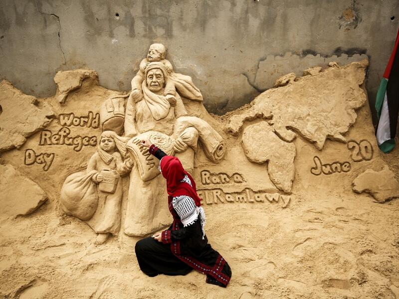 Palestinian sand sculptor Rana Ramlawi finishes a new artwork creation commemorating World Refugee Day, a day dedicated by the United Nations General Assembly to raising awareness of the situation of refugees throughout the world, in Gaza City on June 20, 2020, depicting a woman carrying a child and a sack of flour bearing the logo of the United Nations Relief and Works Agency for Palestine Refugees (UNRWA). MOHAMMED ABED / AFP